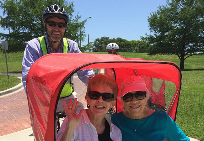 Dr. Keith Whitworth shares a ride with two participants in the Cycling Without Age program, along the Trinity River trail in Fort Worth, Texas.