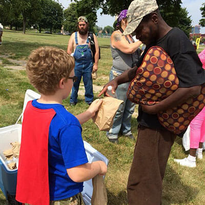 Super Ewan gives a bagged lunch to a homeless man in Roosevelt Park, during one of his first caped "adventures" in Detroit.