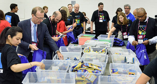 Points of Light Chairman Neil Bush and conference attendees join teamGM Cares to pack backpacks will school supplies for local children.