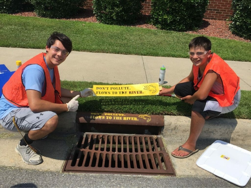 Liam Dao (left) stencils an anti-pollution message on a storm drain with a member of his Paint The Drain team./Courtesy Liam Dao 