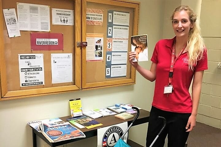 Alicia holding up a copy of Neonatal Abstinence Syndrome: A Guide For Families in front of an AmeriCorps resource table./Courtesy Alicia Nelson