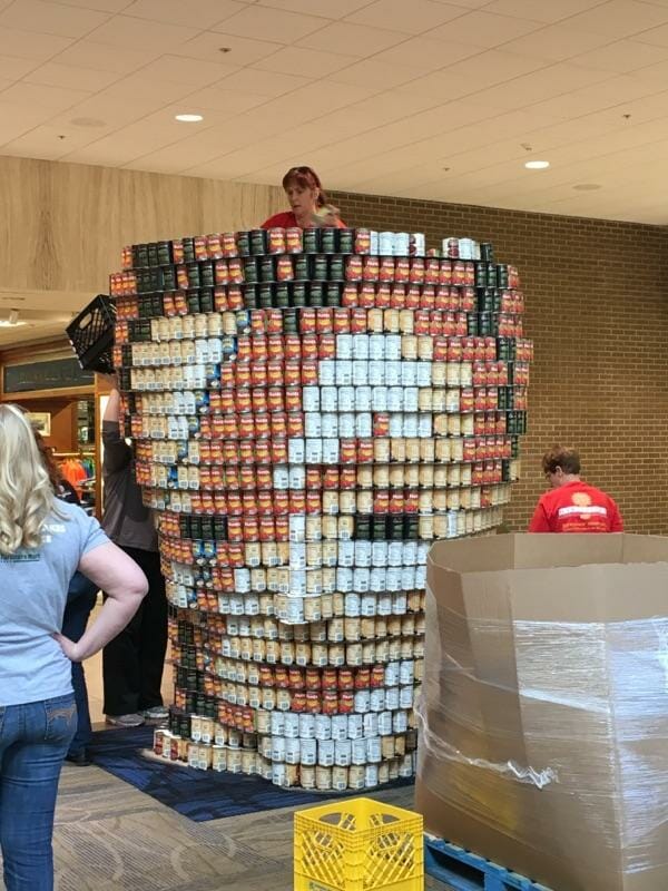 Carrie climbs a ladder behind a sculpture of David Bowie, composed of canned goods, at Harvester's annual DeCANstruction event./Courtesy Carrie Roberson.