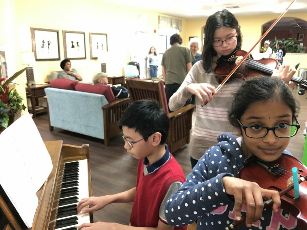 Student volunteers John Christian Dacunos, Brianna Poon, and Sanjana Gokul (left to right) perform for seniors at an assisted care facility in Flower Mound, Texas./Courtesy Karen Lim-Smith