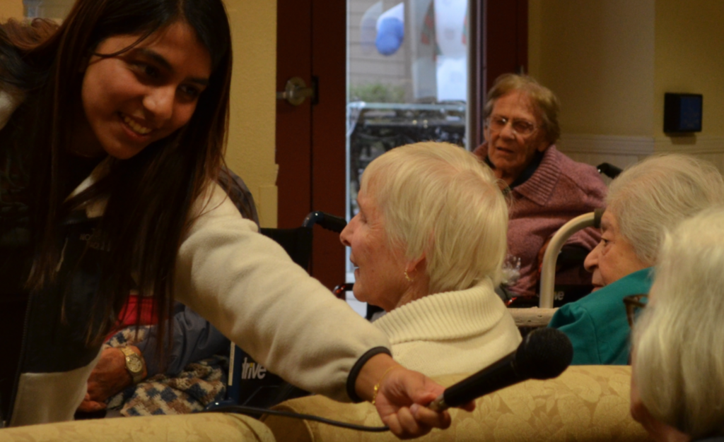 Nishka hands the microphone to a resident of The Terraces of Los Altos in Los Altos, Ca., during a perfomance./Courtesy Nishka Ayyar