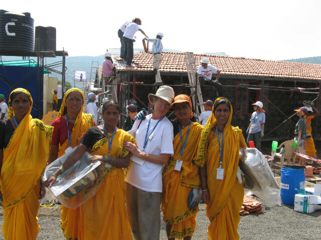 Joyce with a group of Indian women. Two of the women are carrying the sinks that will be installed in their homes. In the background building is taking place./ Courtesy Bob and Joyce Daugherty