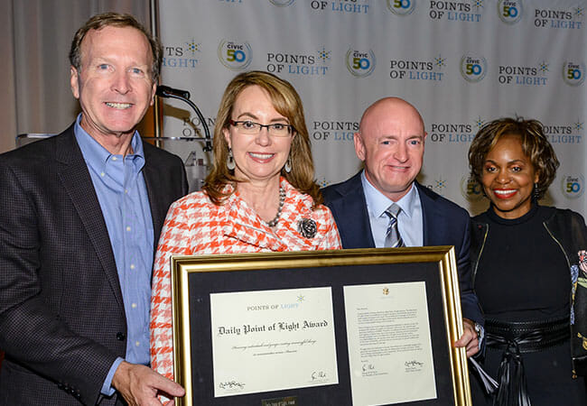 Rep. Gabrielle Giffords and Capt. Mark Kelly received the Daily Point of Light Award at the 2018 Service Unites conference, presented to them by Natalye Paquin, president and CEO of Points of Light, and Neil Bush, board chair for Points of Light.