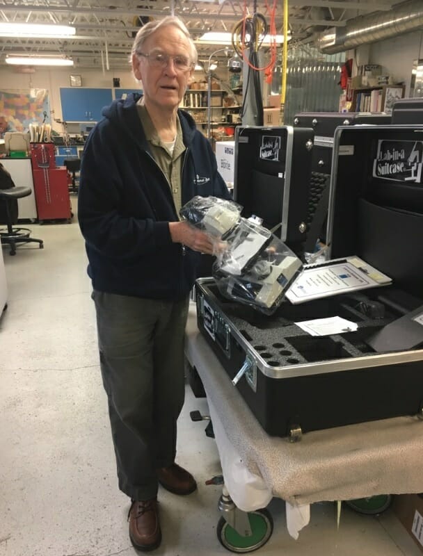 John standing by the microscopes that he works on for the Lab-in-a-Suitcase./Courtesy John Hoekstra 