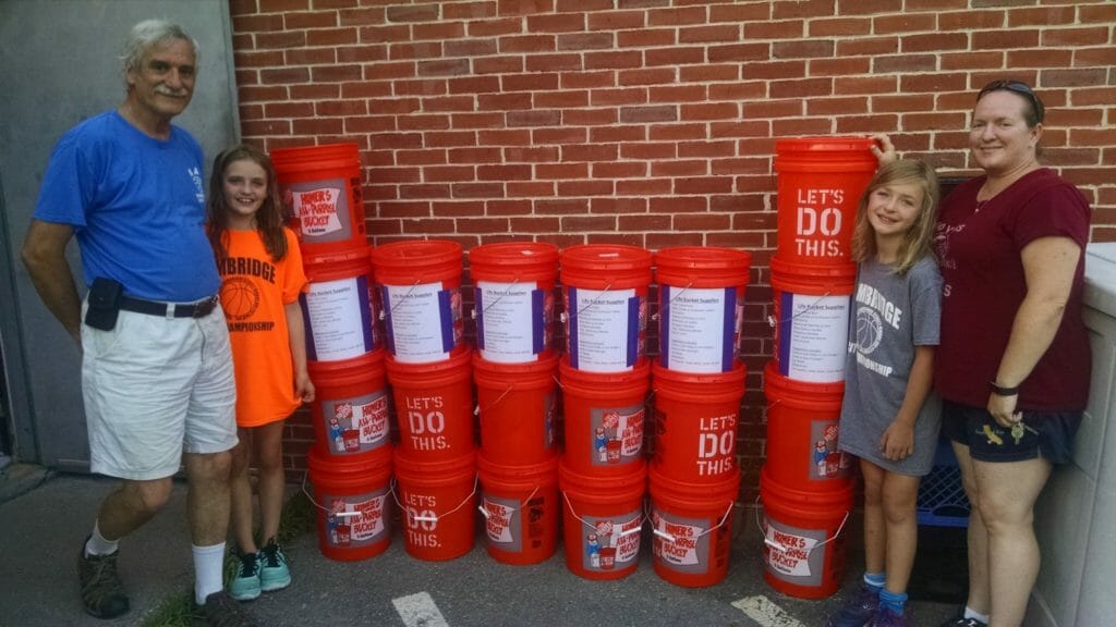 Rebecca and her mother Rachael (R) and friend Lily (left) and Paul, a volunteer for Loaves and Fishes, show off the Life Buckets donated the local food pantry in nearby Devens, MA./ Courtesy Rebecca Fusco