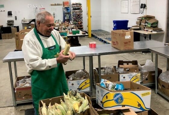 Bob Marshak shucking corn at the food pantry. His volunteer work enables the food pantry to provide struggling families with fresh produce./ Courtesy Bob Marshak 