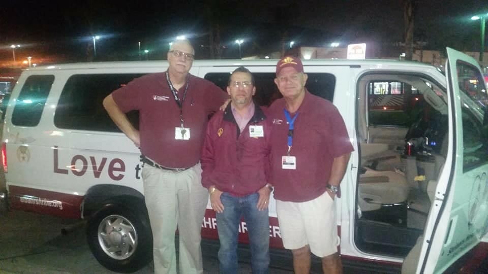 William, left, works with fellow volunteers Alex Ramierez and Mike George in front of the van used to transport children in need to the Shriners for Children Medical Center./ Courtesy William Romer