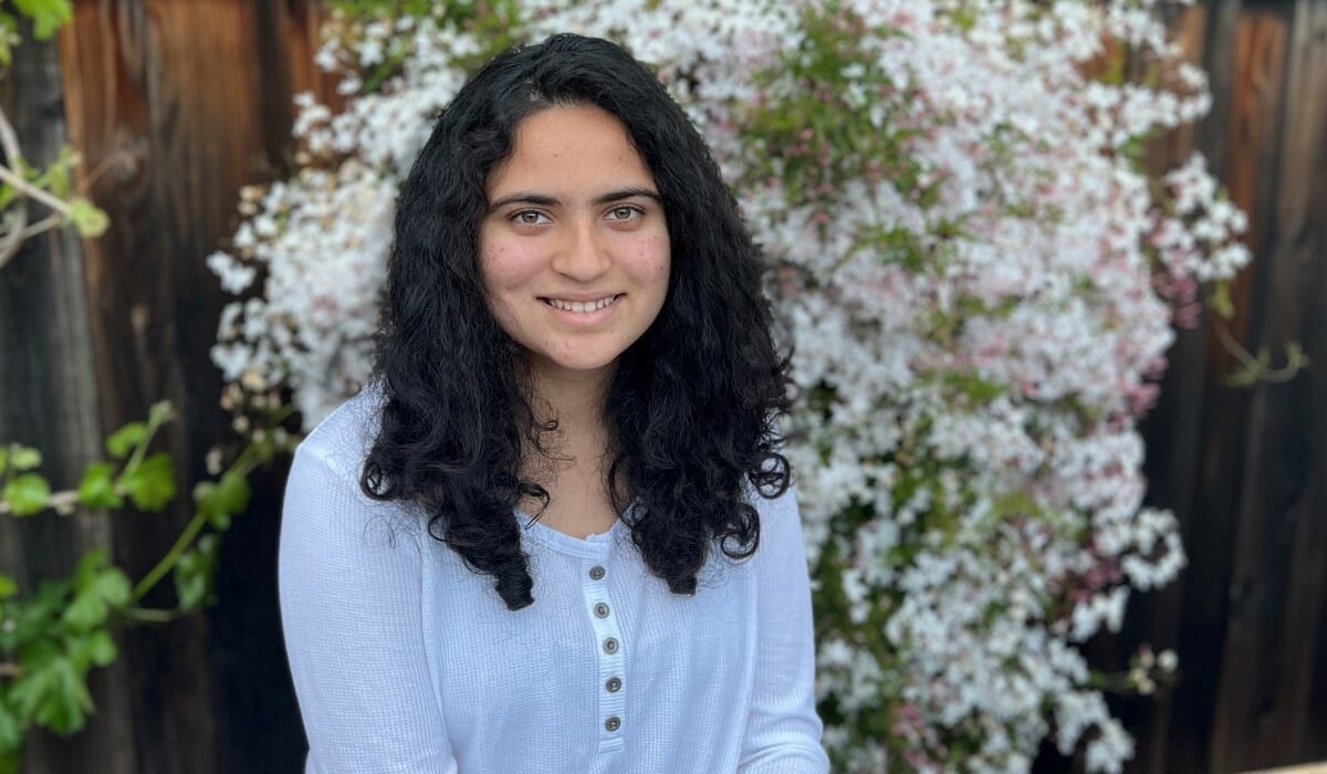 Teenage girl seated smiling in front of a bush with white flowers.