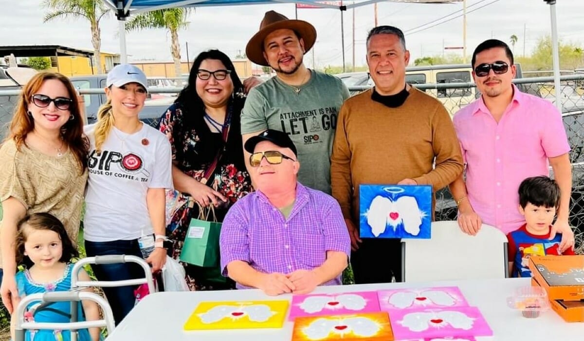 A group of people pose together smiling behind a table displaying paintings