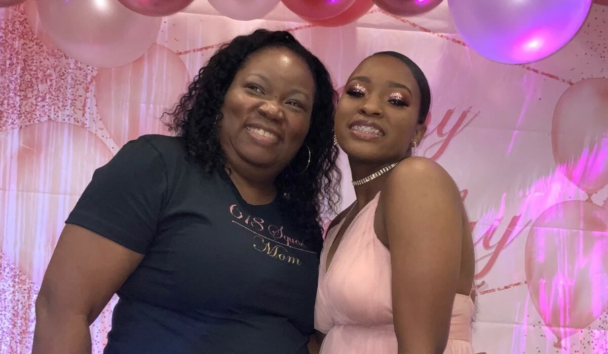 A woman and her teenage daughter stand together smiling.