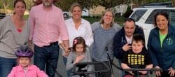 Group of people posing outdoors, with three children on adapted tricycles in the front.