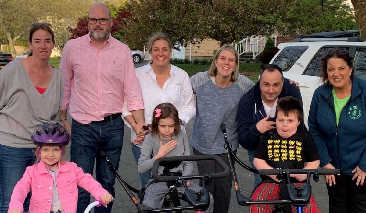 Group of people posing outdoors, with three children on adapted tricycles in the front.