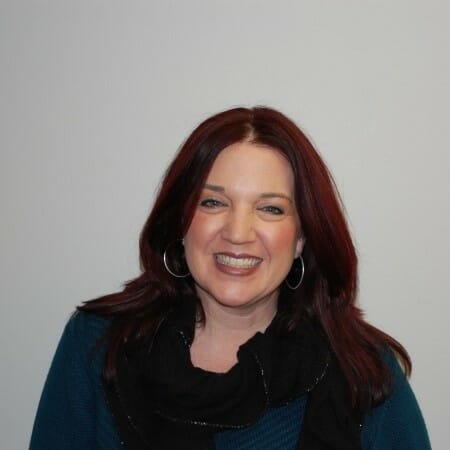 Headshot of a woman with auburn hair wearing a dark green top and blacks scarf