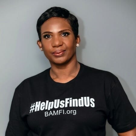Headshot of a woman with short hair wearing a t-shirt emblazoned with the hashtag #HelpUsFindUs