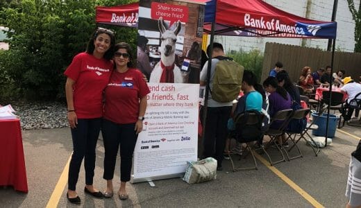 Two women in red shirts standing in front of a Bank of America tent.