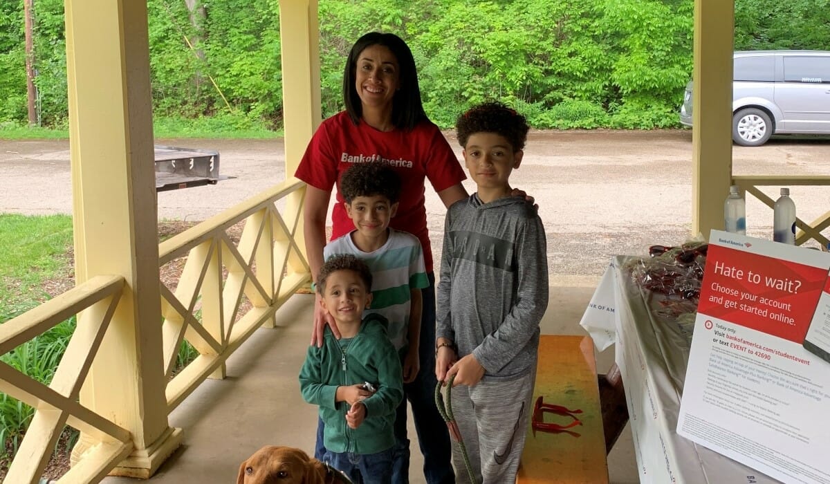 Woman in a red Bank of America shirt poses with kids in an outdoor park shelter.