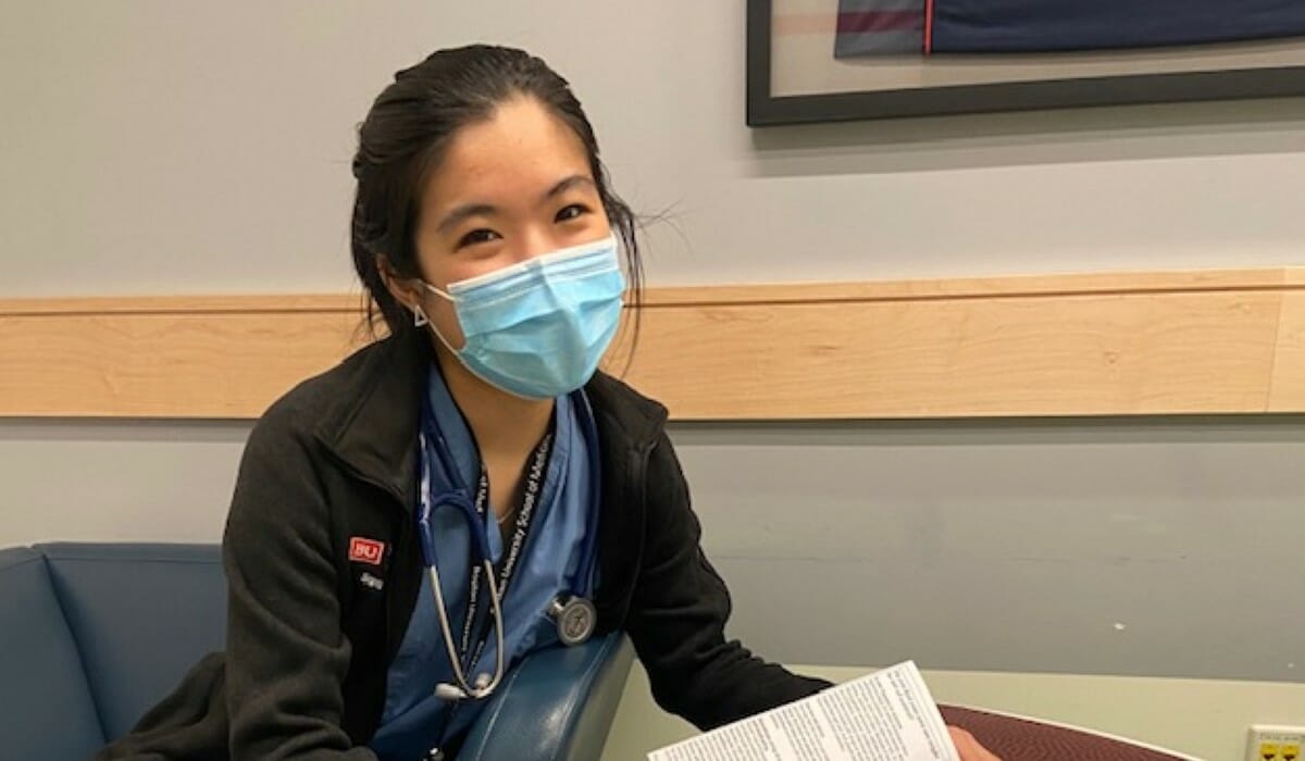 Seated woman in scrubs and a surgical mask with a stethoscope around her neck