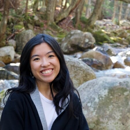 Smiling woman with black hair standing in front of a rocky stream