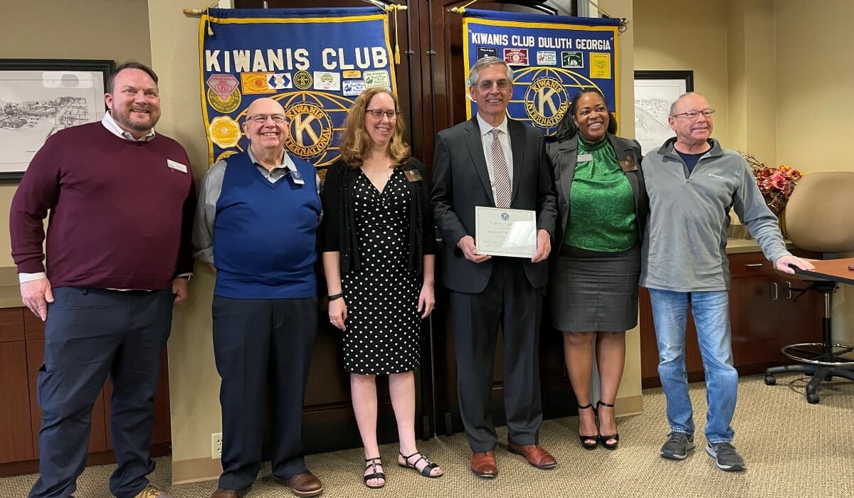 Five people pose together indoors in front of Kiwanis Club banners