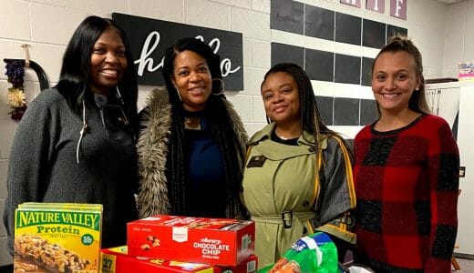 Four women pose with non-perishable food ready to be donated.
