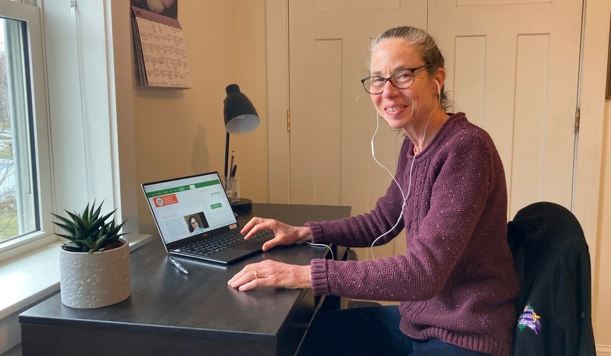 Woman in a purple sweater sits at a desk.