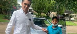 Smiling man and boy fist bump while standing in a driveway.