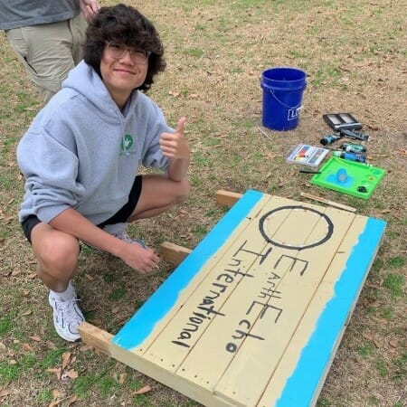 Person crouches on the grass by a hand-painted sign reading "EarthEcho International"