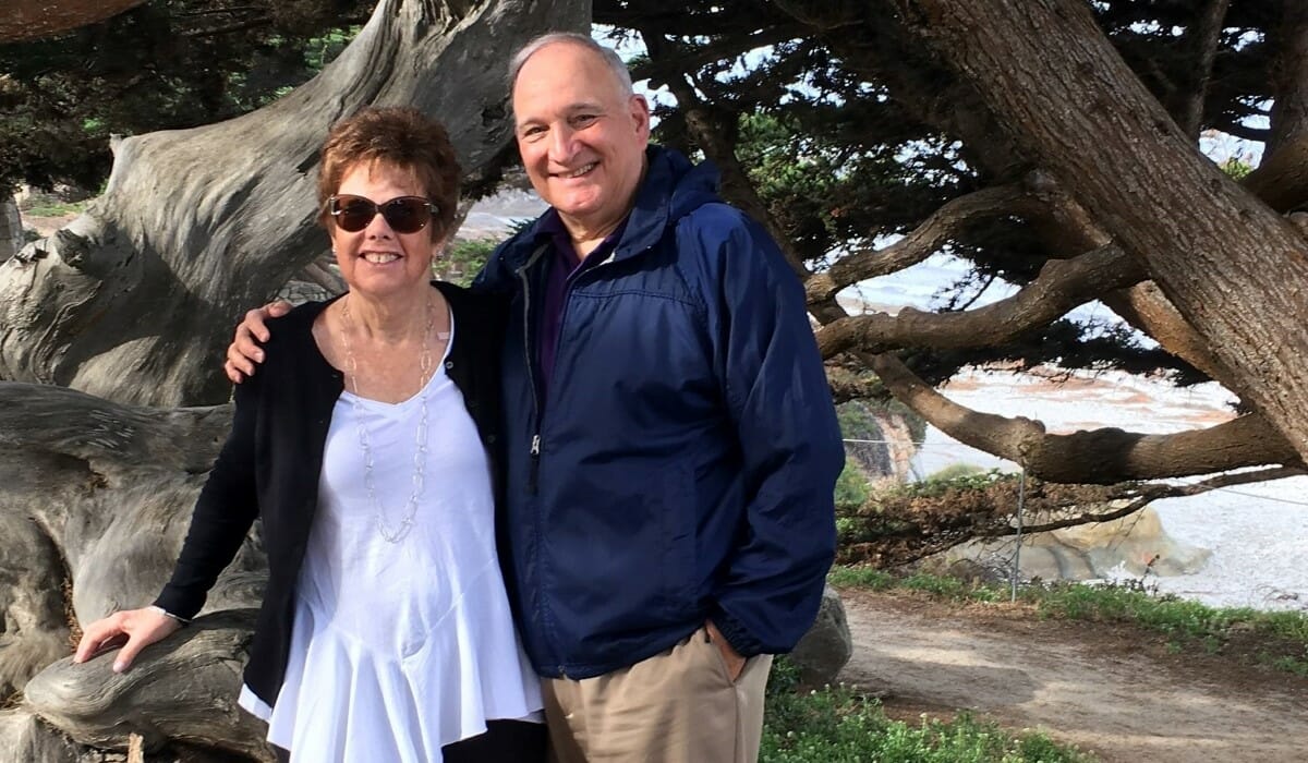 Two people stand together underneath trees.