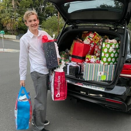 Teenager loads donated Christmas gifts into a car trunk.