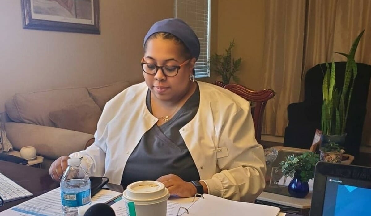 Woman in glasses sits working at a table.