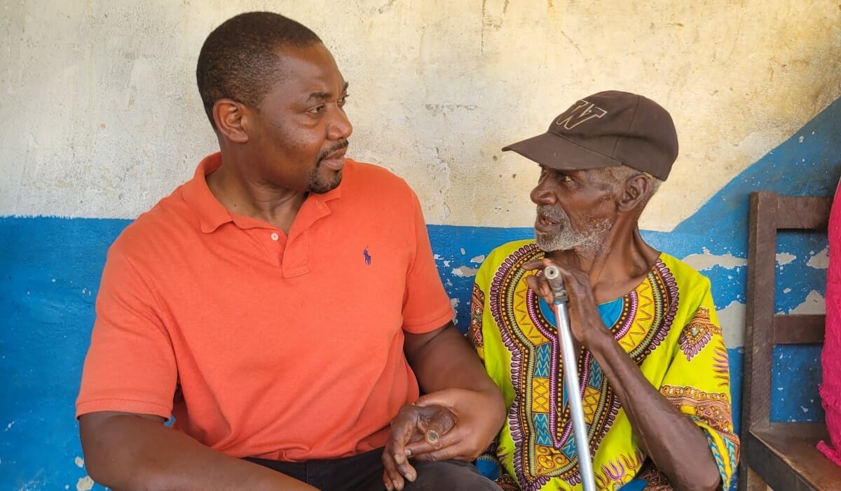 Two men, one holding a cane, sit together