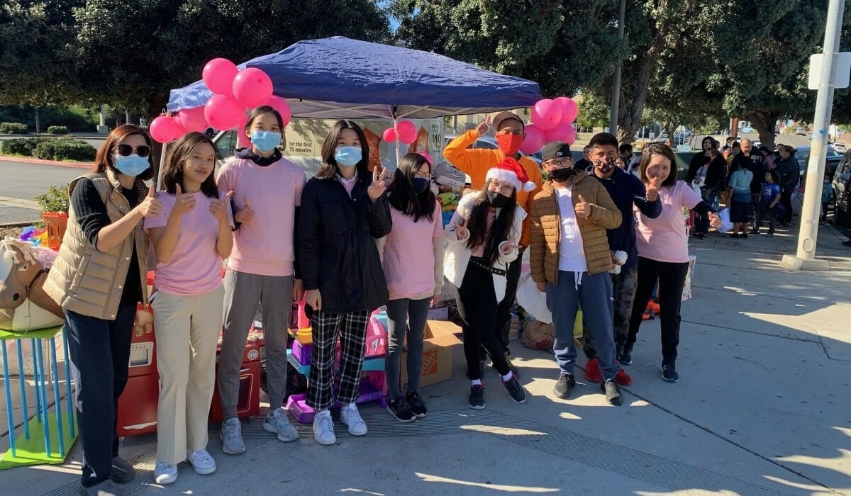 Group of people pose outdoors in front of a frame tent with pink balloons.