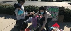 Teenage girl crouches down to hand some toys to another girl from a large pile of toys.