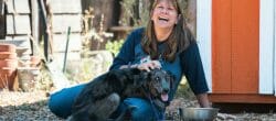 Woman sits on the ground laughing with a large dog on her lap.