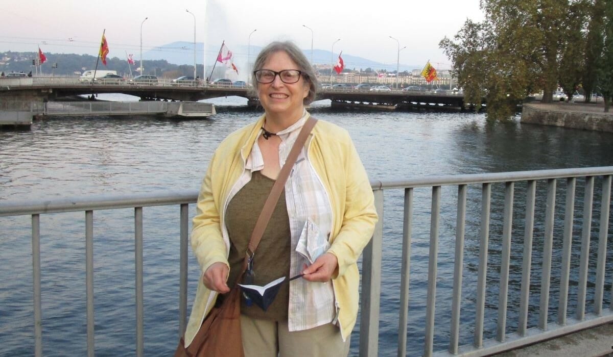 Woman standing in front of the water with a bridge in the background.