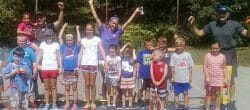 Group of adults and children pose on a tennis court.