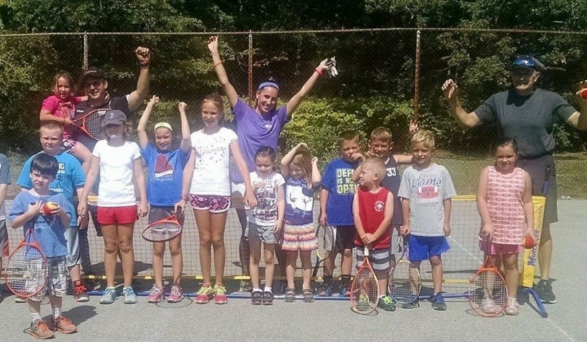 Group of adults and children pose on a tennis court.