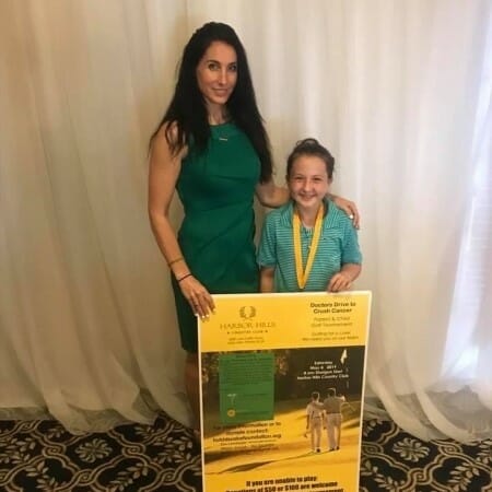 Woman and daughter stand with an advertisement for a charity golf tournament.