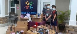 Group of boys standing in front of a house behind pile of boxes filled with donated items.