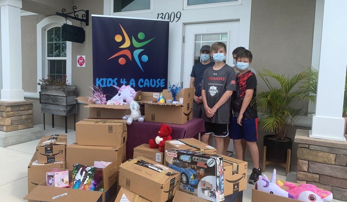 Group of boys standing in front of a house behind pile of boxes filled with donated items.