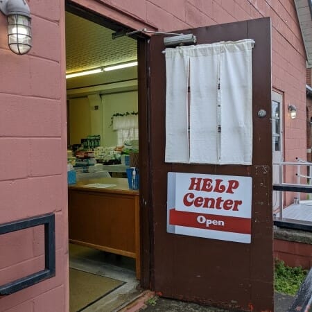 Outside of a red building with an open door with a sign reading "Help Center: Open"