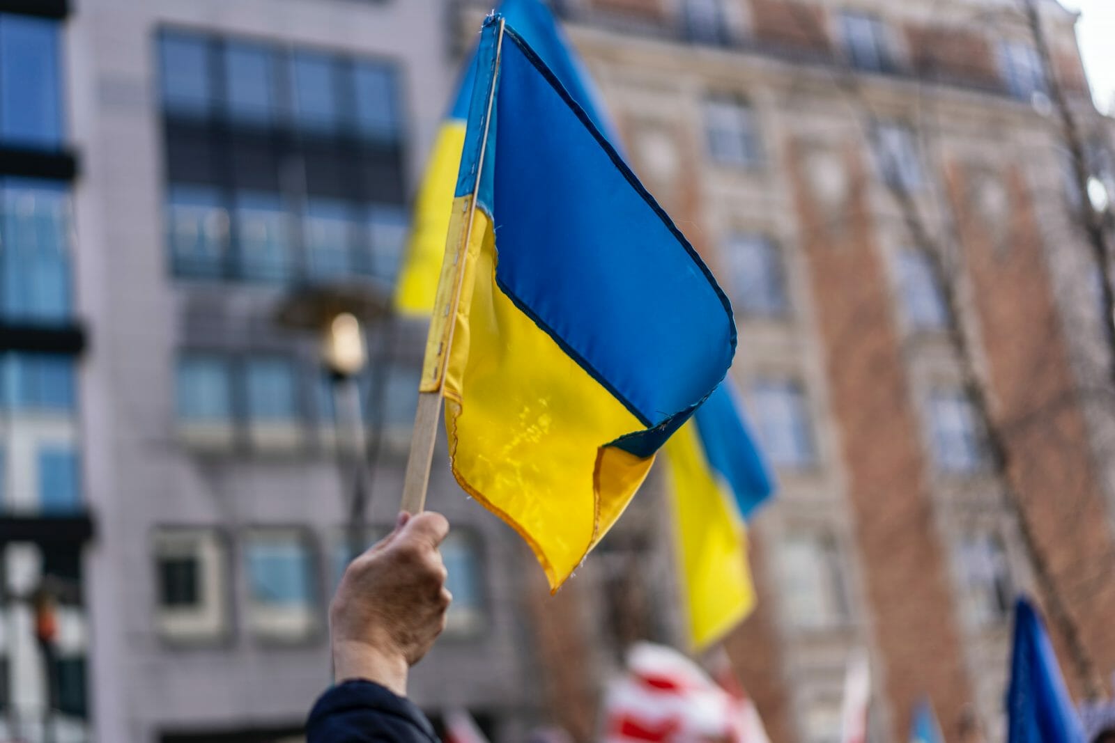 Hand holding Ukrainian flag with cityscape in background