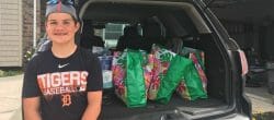 Teenager sits on the open trunk of a car loaded with bags of items to be donated.