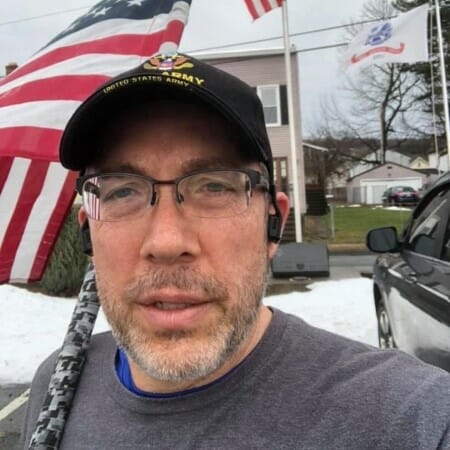 Selfie of a man wearing a US Army baseball cap and carrying an American flag