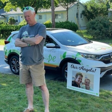 Man stands on a yard in front of a car.