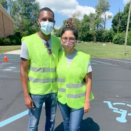 Two people stand together in a parking lot wearing reflective vests.