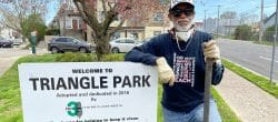 Man holding a shovel standing next to a sign that reads "Triangle Park"